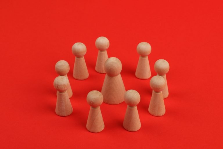 Wooden figurines arranged in a circle on a vibrant red backdrop, creating a crafted minimalist still life.