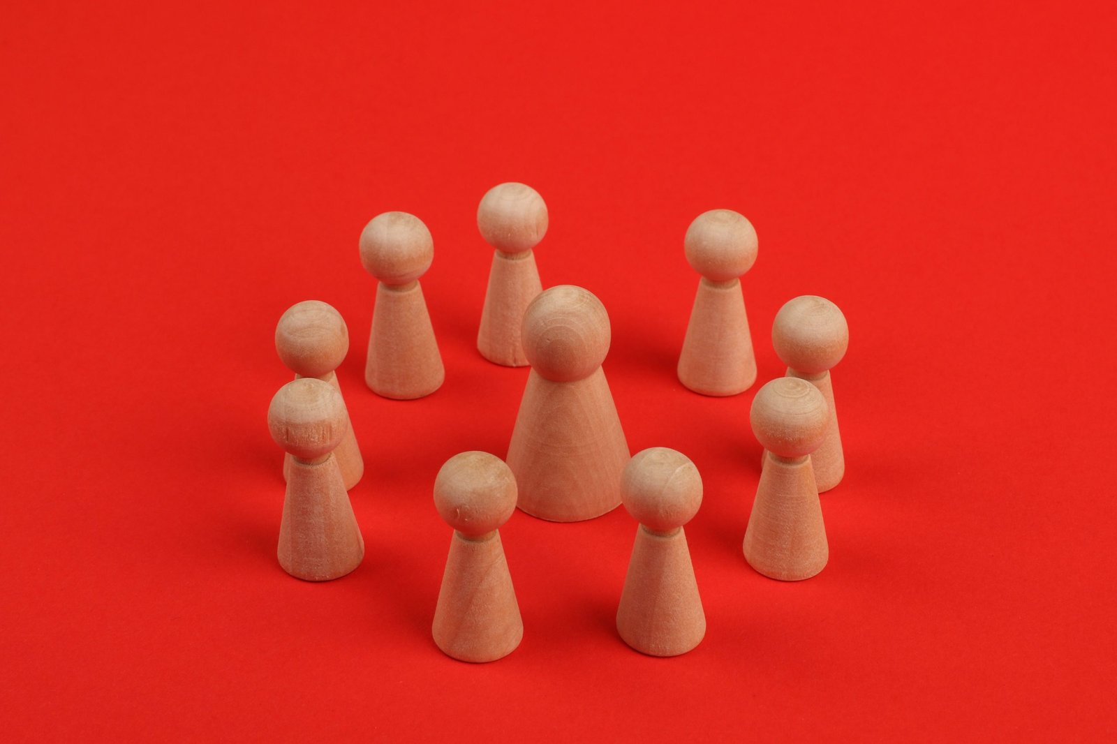 Wooden figurines arranged in a circle on a vibrant red backdrop, creating a crafted minimalist still life.